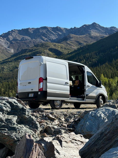 Experience van life! White RV rental parked at a rugged Alaska mountain viewpoint, open doors invite adventure.