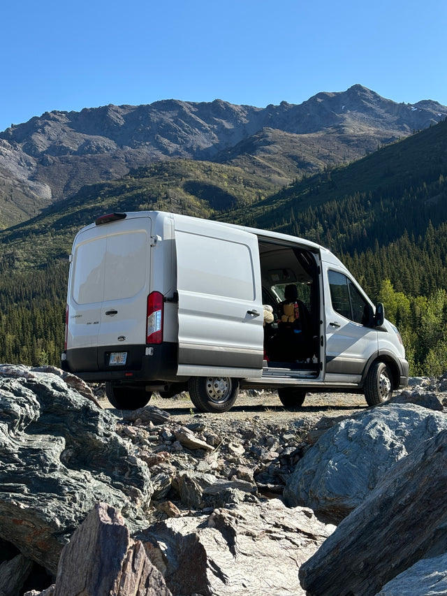 Experience van life! White RV rental parked at a rugged Alaska mountain viewpoint, open doors invite adventure.