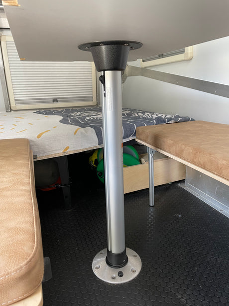 RV rental interior showcasing a versatile dining table, built-in benches with storage, window blinds, and a durable floor.