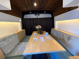 Cozy RV rental dinette with cards, coffee, and flowers on a wooden table, featuring comfortable bench seating for van life adventures.