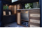 This RV rental interior showcases custom wood cabinetry, a stainless steel fridge, microwave, and comfortable sofa/bed.