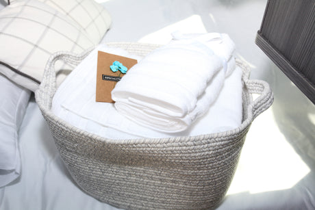 RV rental amenities: A woven basket holding fresh white towels and a welcome card on a cozy bed. Enjoy comfort on your trip.
