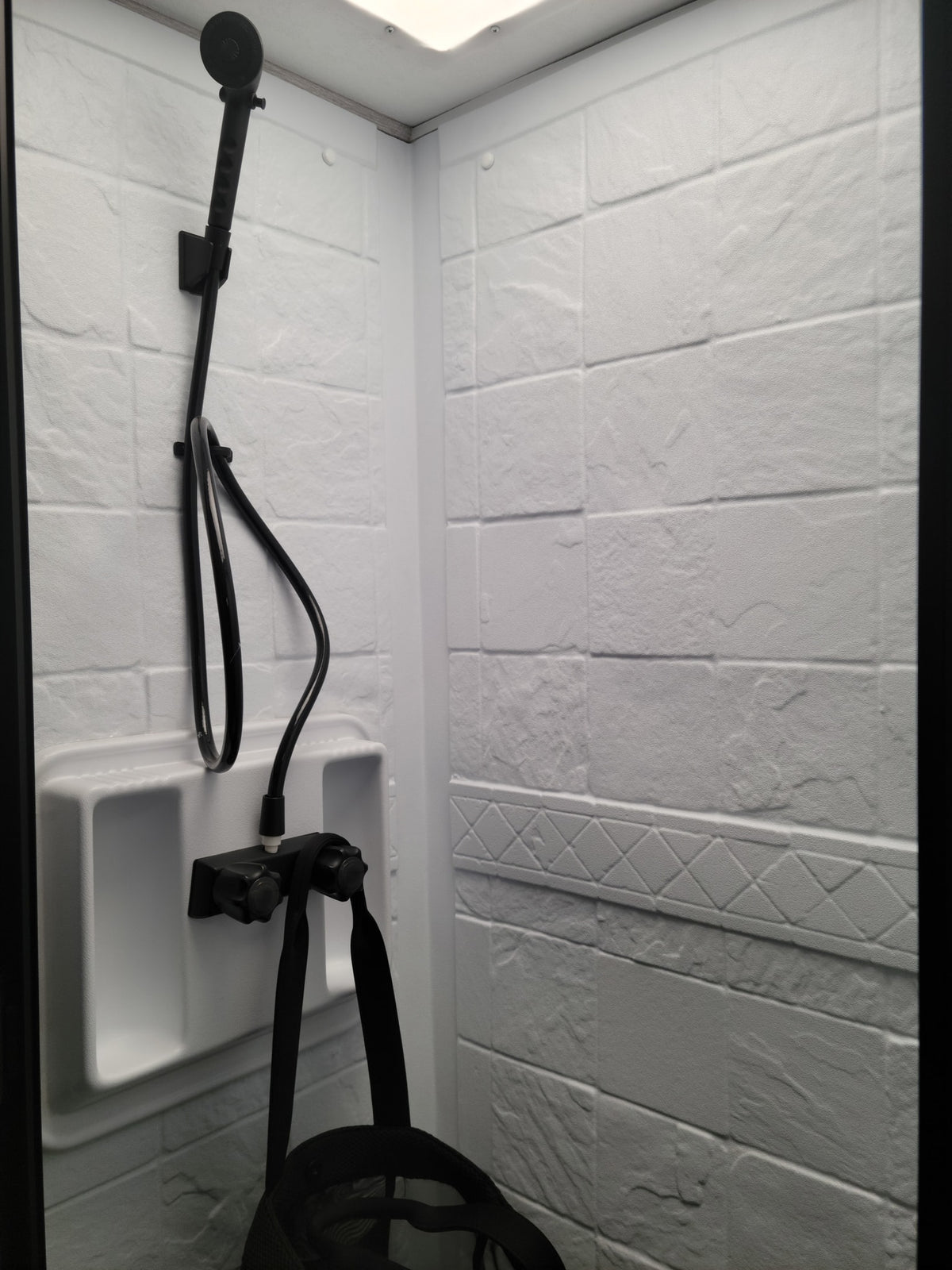 Compact RV rental shower: white textured walls, black handheld showerhead, and controls. Clean, functional bathroom for travel. — photo 9