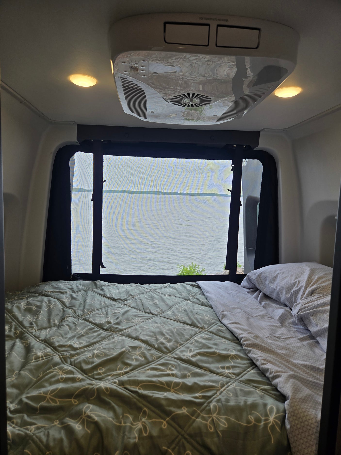Cozy RV rental bedroom with lake views through a screened window, featuring a comfy bed and AC unit.