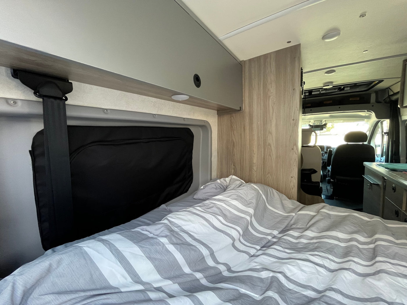 Cozy interior of an RV rental: a bed with striped bedding, overhead storage, and the front cabin of this camper van. — photo 12
