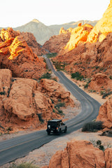 An RV rental, a gray truck with a pop-top, winds through vibrant red rock canyons on a scenic desert road trip.