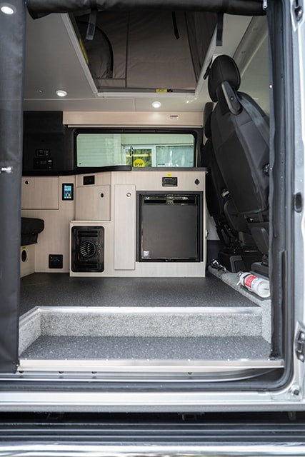 An RV rental's inviting interior: looking into a camper van with a compact kitchen, fridge, control panel, and a step up. — photo 10