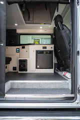 An RV rental's inviting interior: looking into a camper van with a compact kitchen, fridge, control panel, and a step up.