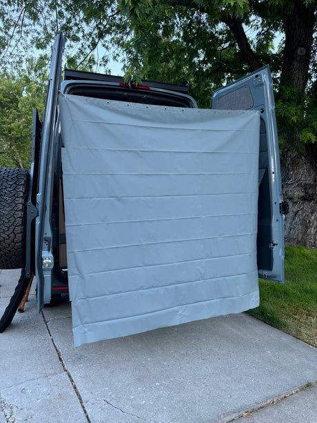 Gray privacy curtain on an RV rental campervan, attached to open rear doors for an outdoor shower setup.