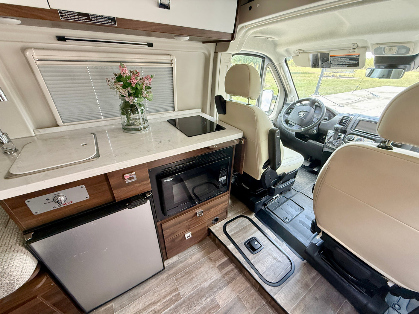 Exploring a compact RV rental's interior: a functional kitchen with sink, stove, microwave, fridge, and the driver's cab. — photo 5