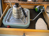 Compact RV rental cooking setup in a drawer: portable stove with kettle, propane tank, and mitt for easy camp meals.