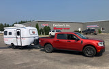 Red truck towing a white Scamp travel trailer, ideal for an rv rental, parked at Eveland's Scamp Trailers business.
