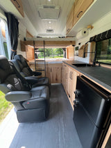 Spacious RV rental interior: bunk beds, kitchen, & comfy black leather captain's chairs. Ready for adventure.