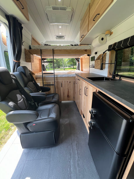 Spacious RV rental interior: bunk beds, kitchen, & comfy black leather captain's chairs. Ready for adventure.