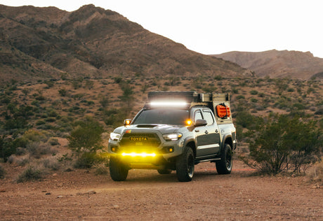 Rugged Toyota Tacoma overlanding truck with bright lights in desert mountains. Explore with this unique RV rental!