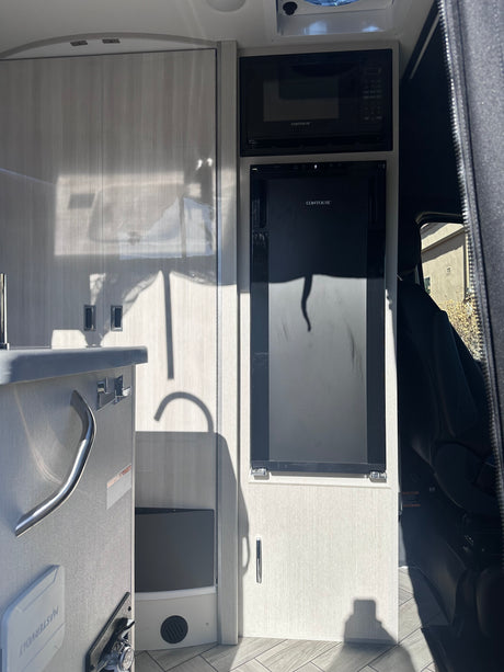 Inside an RV rental: bright galley with a chrome faucet, grey speckled countertop, and covered sink. Side door open to street view.