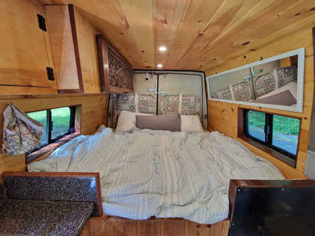 An inviting RV rental interior with a cozy bed, natural wood walls & ceiling, and handy storage for your next adventure.