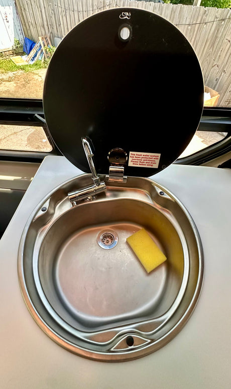 RV rental compact stainless sink with folding faucet. Warning label for fresh water system anti-freeze. Yellow sponge.