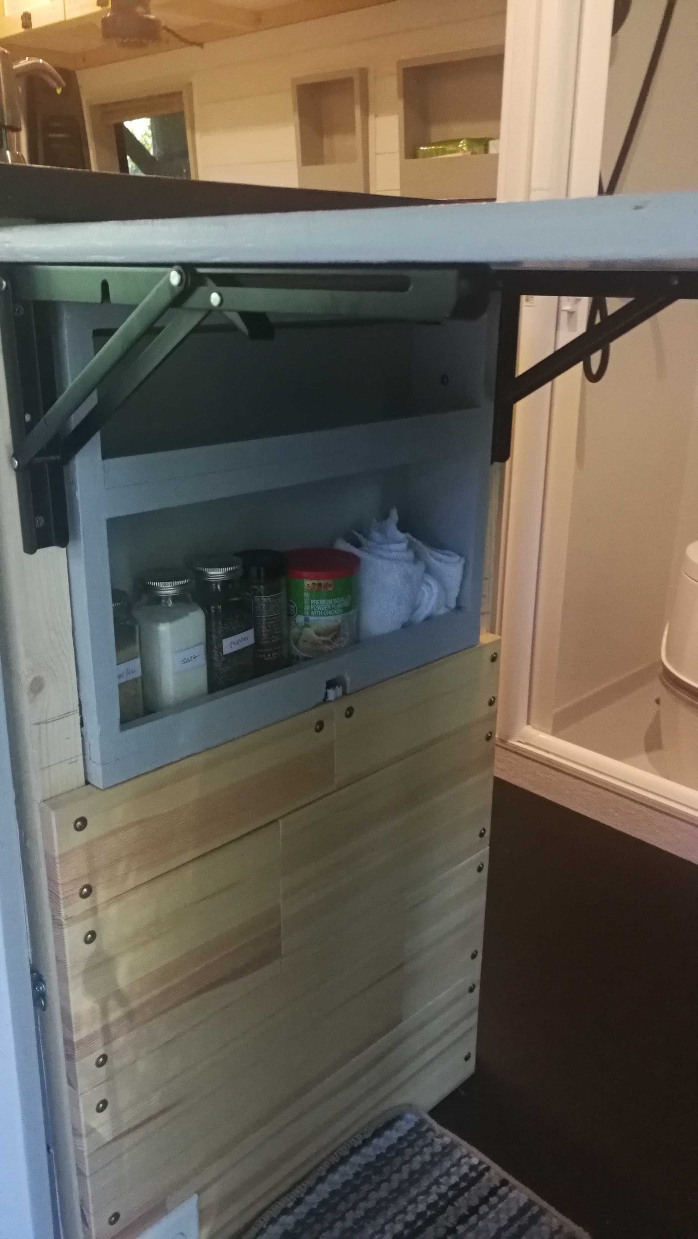 RV rental: Small kitchen area with spice shelf, folded towels, and a collapsible counter-table for efficient use of space.