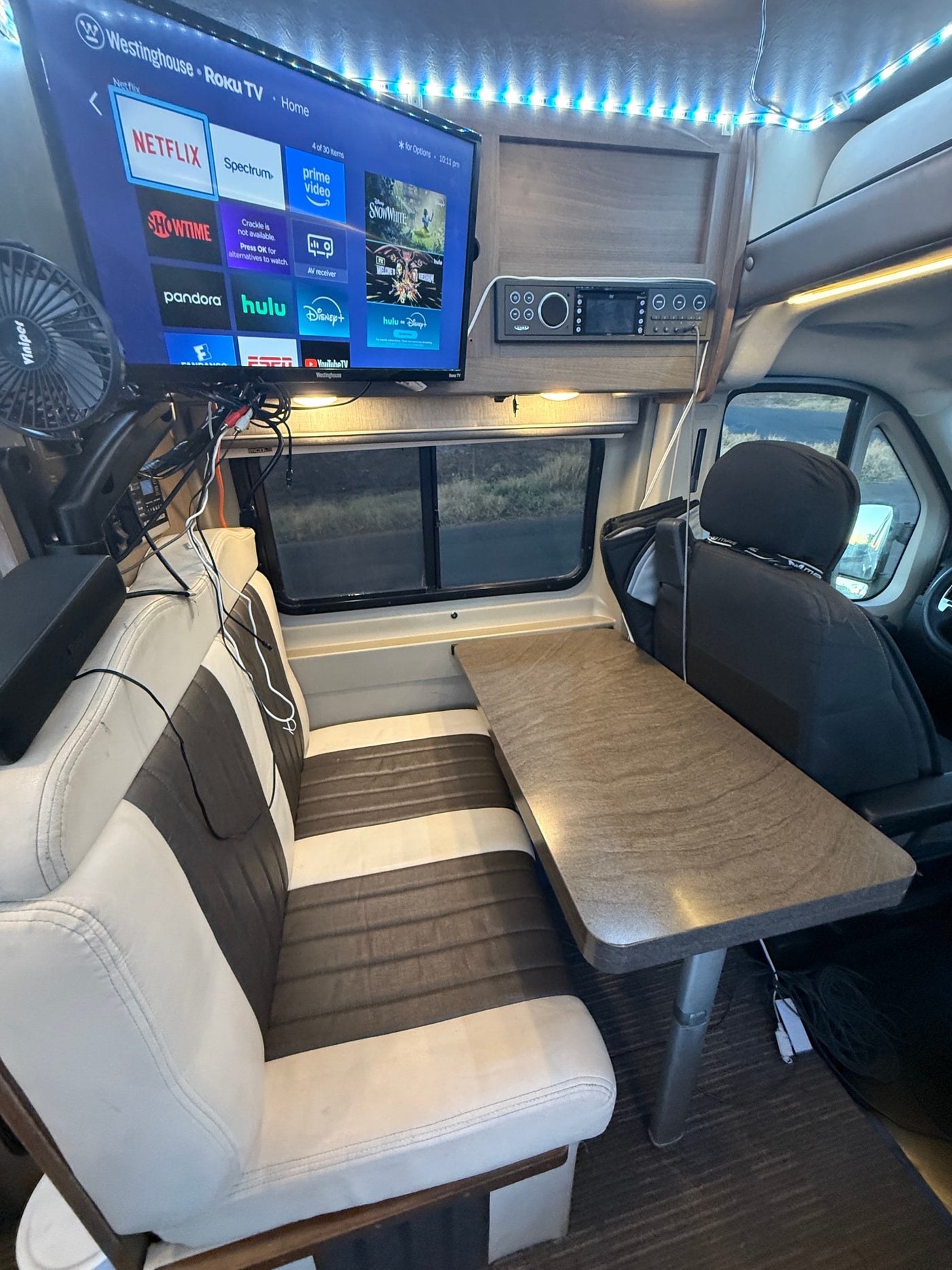 Cozy RV rental interior features a Roku TV for entertainment, a dining table, and comfy bench seating. — photo 13