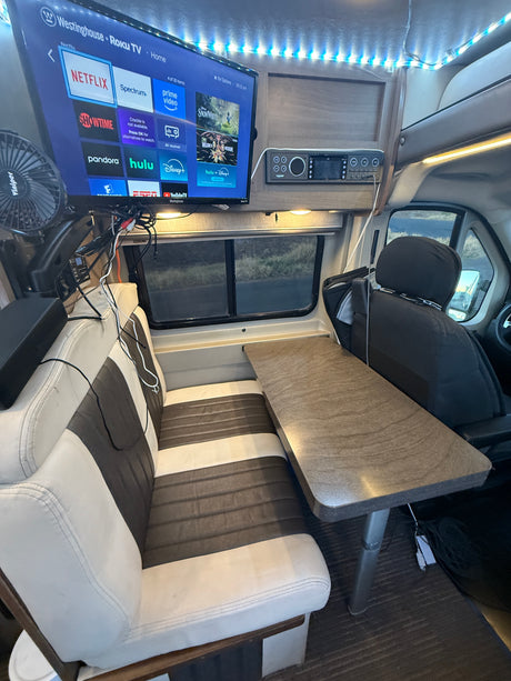 Cozy RV rental interior features a Roku TV for entertainment, a dining table, and comfy bench seating.