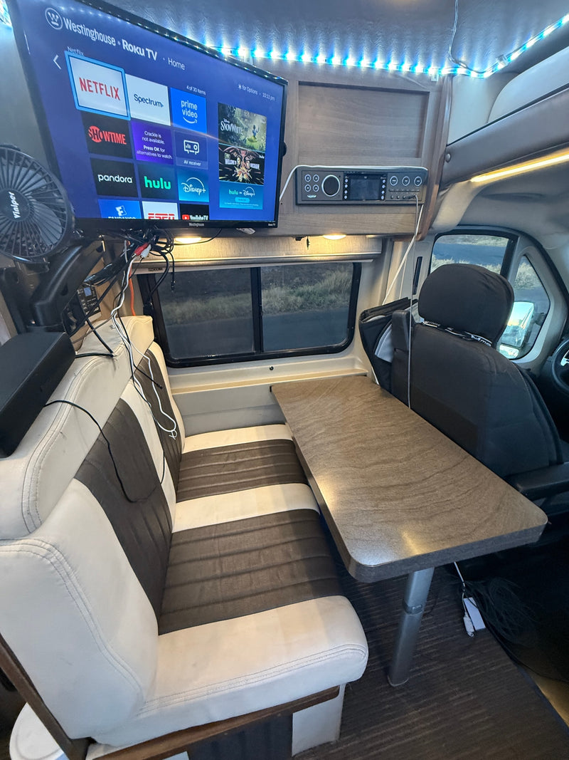 Cozy RV rental interior features a Roku TV for entertainment, a dining table, and comfy bench seating. — photo 13