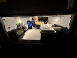 Organized RV rental interior: well-lit with camping gear, storage boxes, and a table, ready for adventure.