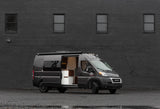Stylish grey camper van, side door open to reveal a modern kitchen, ready for your RV rental journey. Parked by a dark wall.