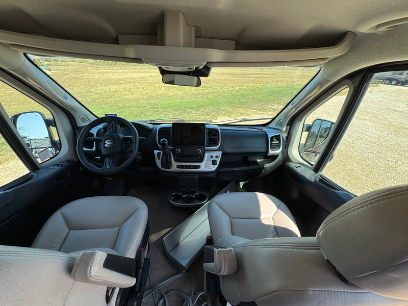Inside an RV rental van, showing the cockpit with steering wheel, dashboard, and light-colored front seats looking out to a field. — photo 4