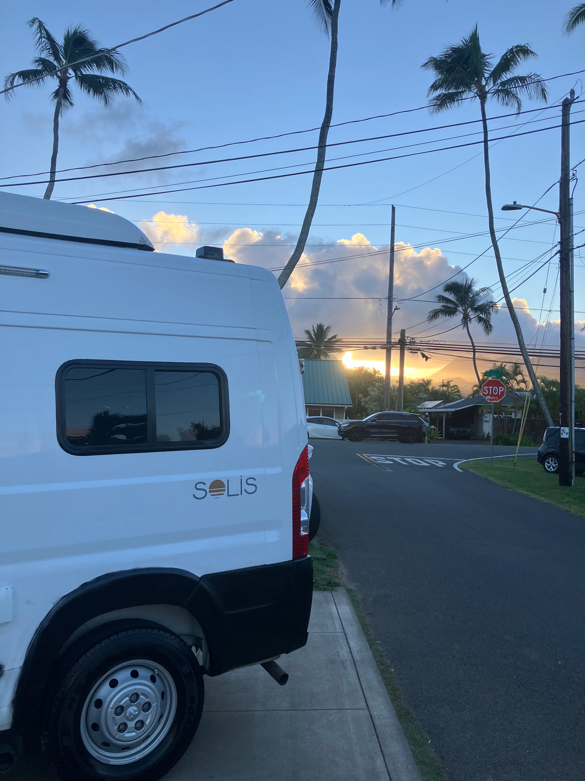 White Solis rv rental parked on a tropical street at sunset, with vibrant clouds, palm trees, and utility poles. — photo 7