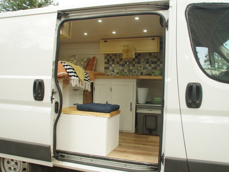  parked on a dirt road against a backdrop of mountains and pine trees.|Open door of a white RV rental revealing its inviting interior: bed — photo 2