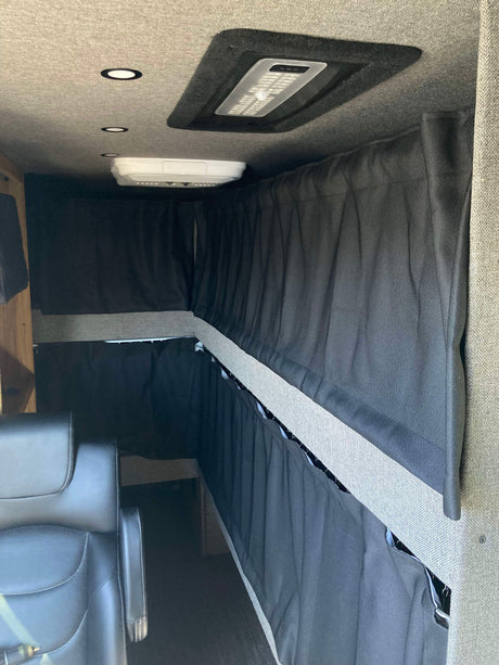 RV rental interior setup with dark privacy curtains for bunk beds, overhead lights, and a comfortable seat.