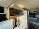 This RV rental features a bright, compact interior with open wood cabinets, neatly folded towels, a sink, and a comfortable bed.