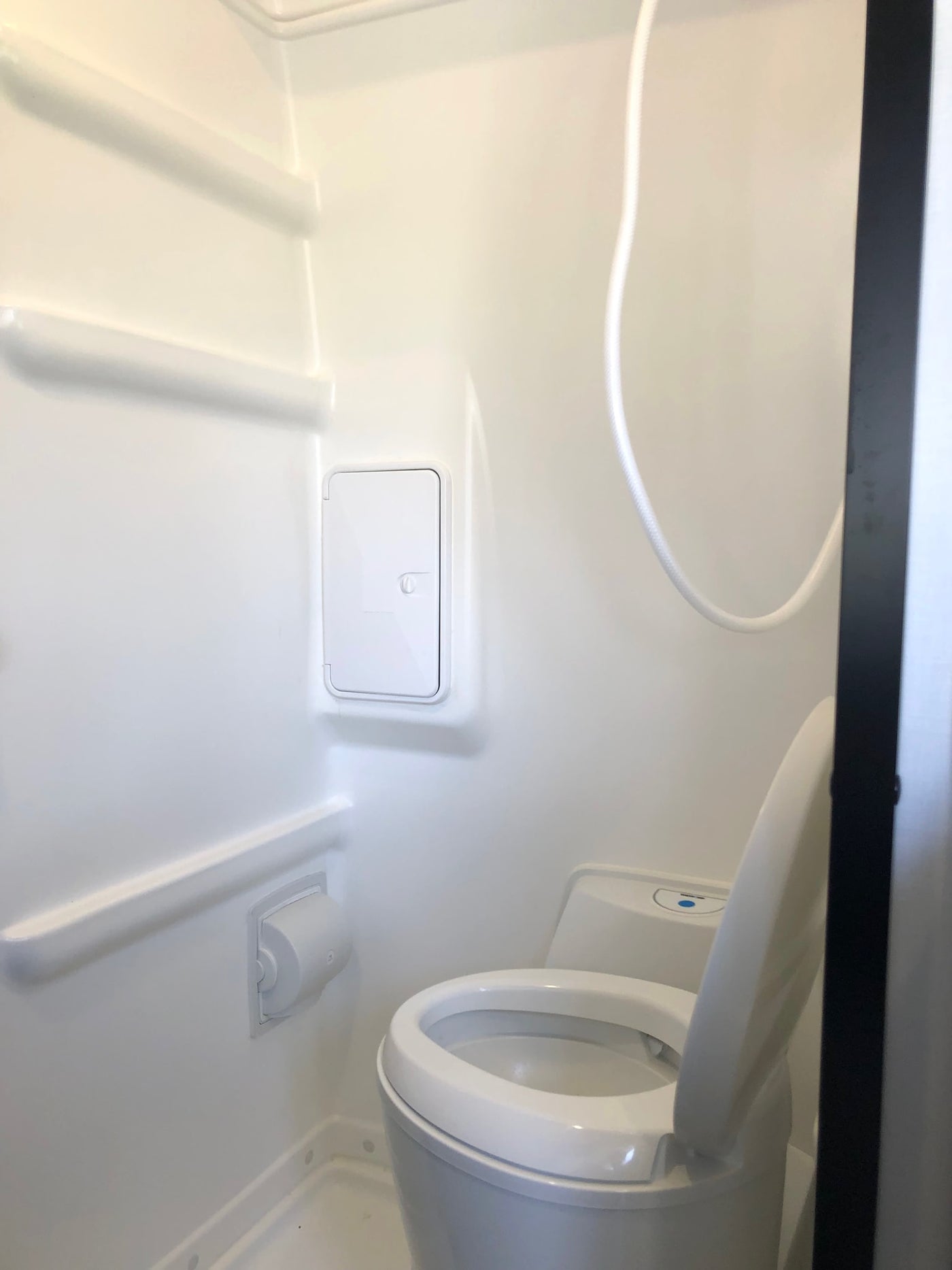 Compact white RV rental bathroom featuring a toilet with open lid, shower hose, and built-in shelving, ready for use. — photo 15