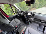 Spacious RV rental front cabin, featuring a modern dashboard, steering wheel, and comfy seats. View of green trees outside.