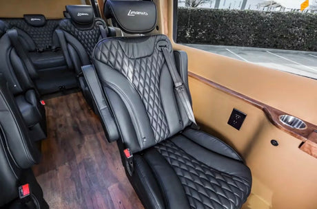 Luxury RV rental interior featuring black leather diamond-stitched captain's chairs, wood floor, power outlets, and cup holders.