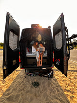 Family bonding in their RV rental. A woman and child sit barefoot, conversing in the open back of their van on the sand.