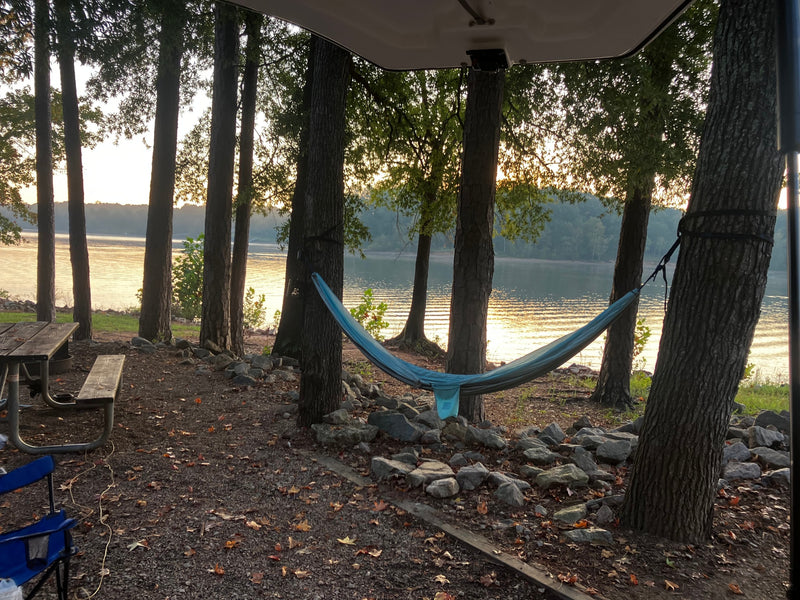 RV rental campsite by a lake, featuring a blue hammock, picnic table, and golden sunrise on the water. — photo 3