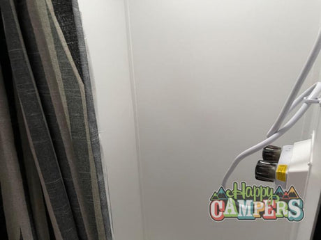 RV rental interior: A textured gray striped curtain hangs on the left, beside a white wall with wall-mounted electrical controls on the right.
