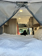 Inside an RV rental: a comfy bed leading to the camper van's bright cabin and front seats. Ideal for road trips!