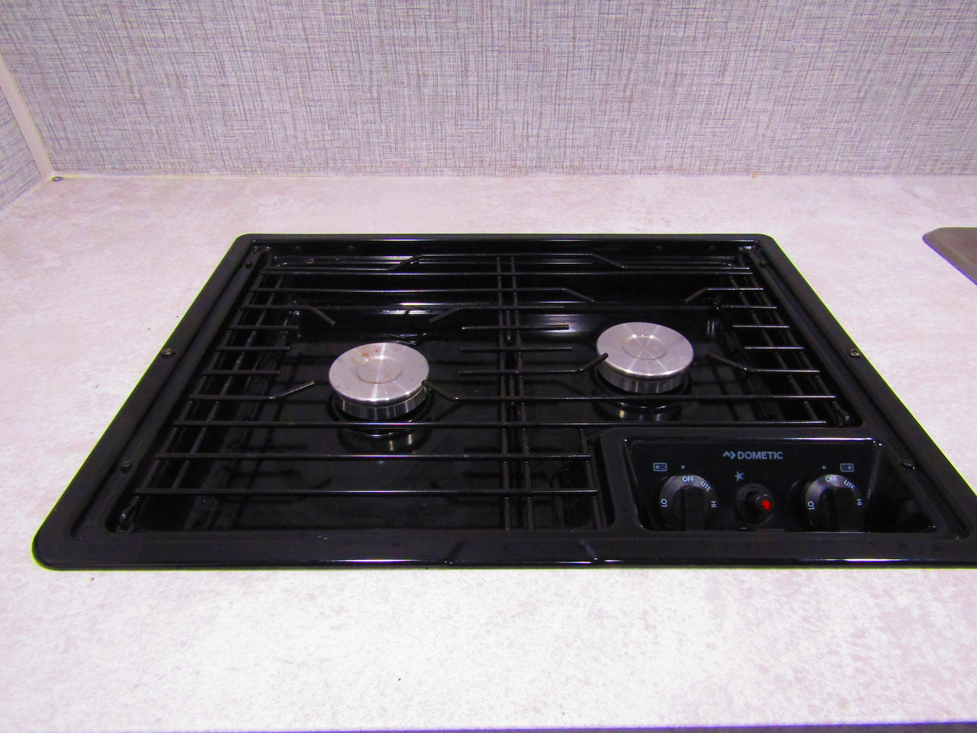 A Dometic two-burner stovetop, integrated into a light countertop, is ready for cooking in this RV rental kitchen.