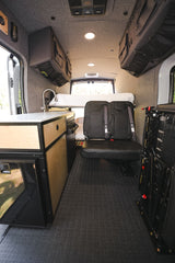 Spacious RV rental camper van interior showcasing a kitchen counter, cozy bed, and rear passenger seats.