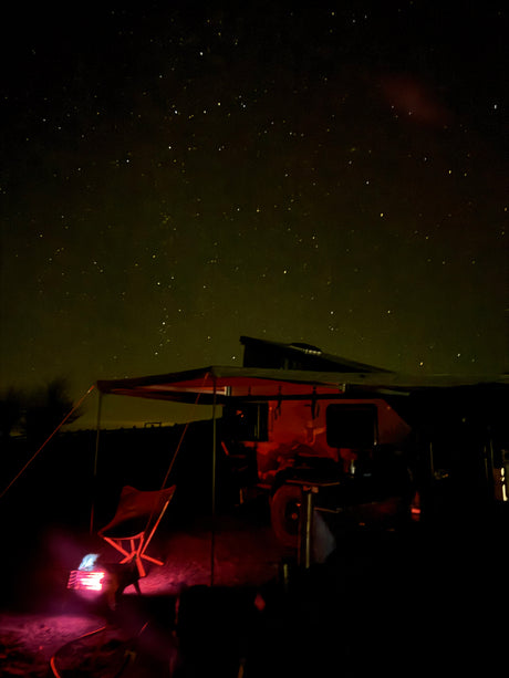 Experience remote stargazing with an RV rental. A camper and chair glow red under a brilliant, star-filled night sky.