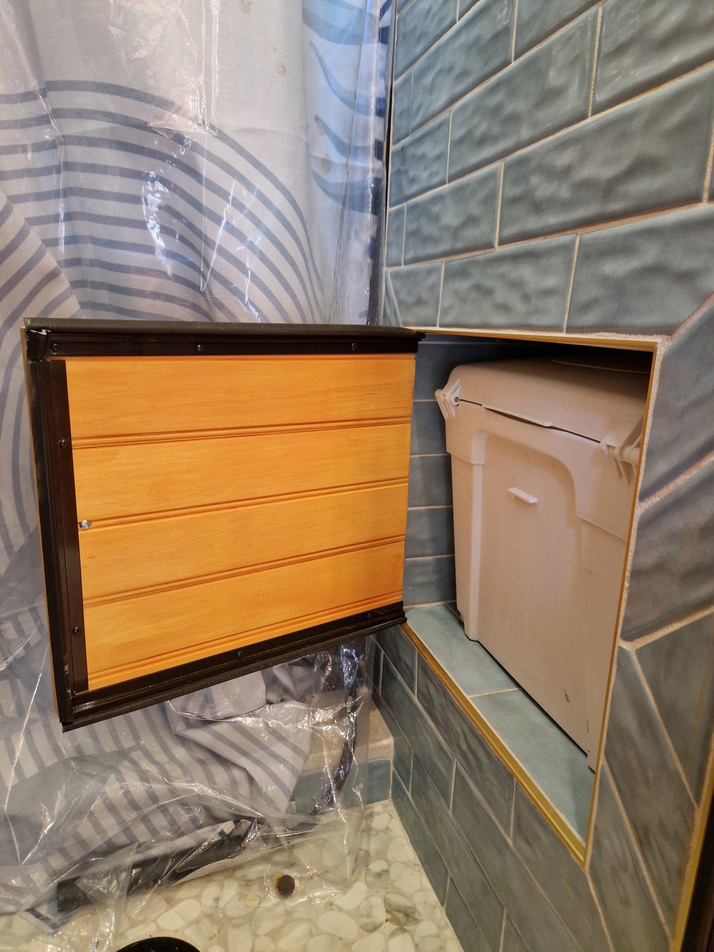 RV rental shower: clever access panel opens to reveal a built-in storage bin within tiled walls.