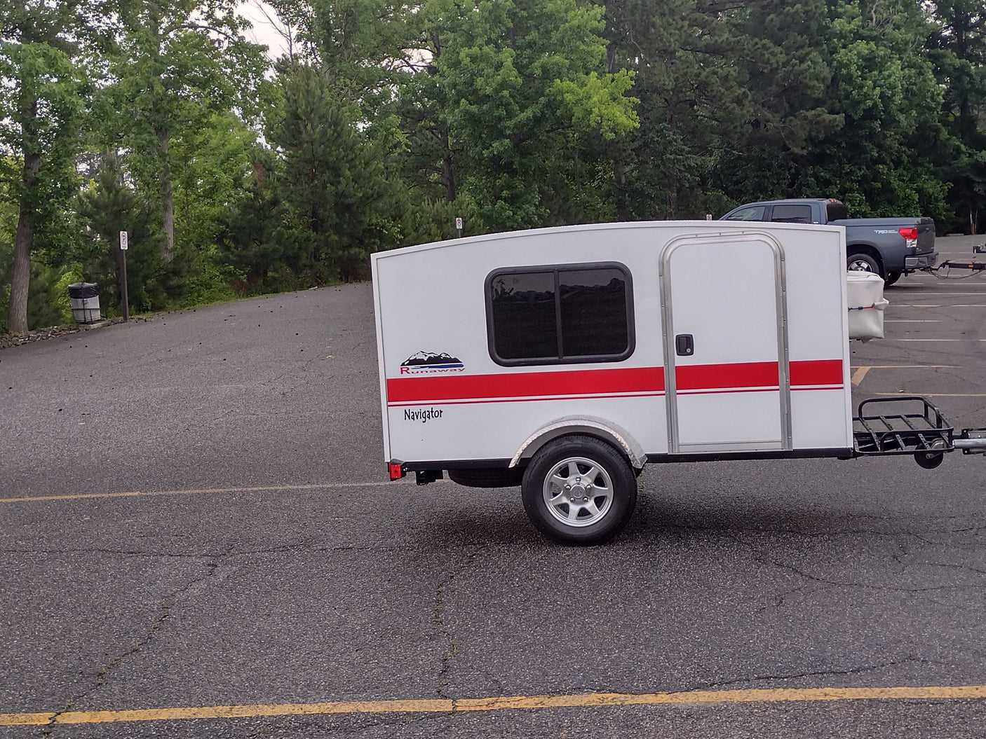 White Runaway Navigator travel trailer. This compact camper offers a minimalist RV rental experience, parked on asphalt.