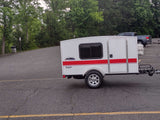 White Runaway Navigator travel trailer. This compact camper offers a minimalist RV rental experience, parked on asphalt.