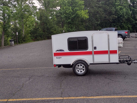White Runaway Navigator travel trailer. This compact camper offers a minimalist RV rental experience, parked on asphalt.