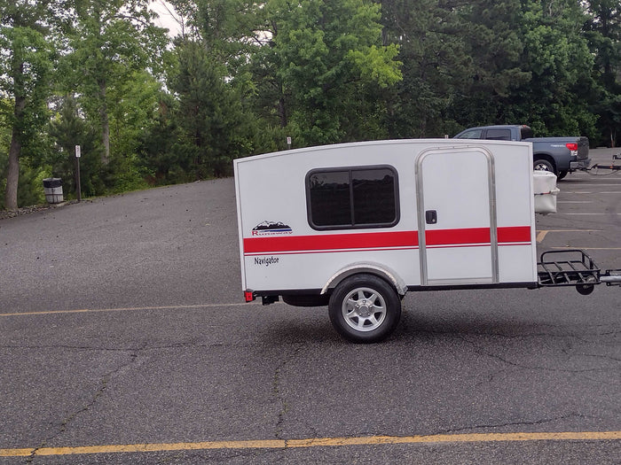 White Runaway Navigator travel trailer. This compact camper offers a minimalist RV rental experience, parked on asphalt.