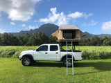 White truck with rooftop tent, ready for RV rental adventures. Camp in green fields with mountains in background.