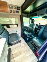 Experience freedom in this spacious RV rental camper van interior. Front seats swivel, lounge area, and control panel visible.